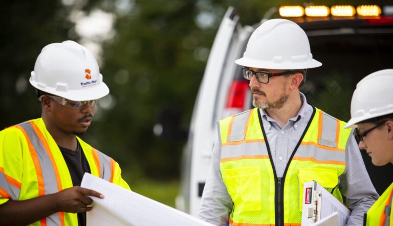 three members of the traffic plan team reviewing a document in front of vehicle