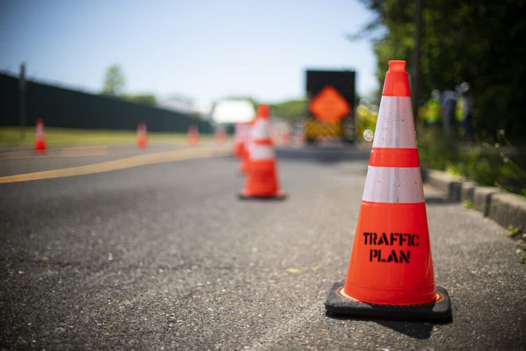 traffic cone with traffic plan sprayed on it sitting on blacktop surface next to foliage