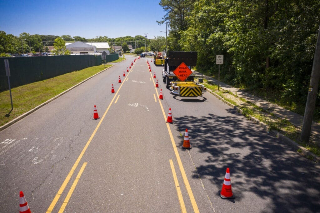 tma truck parked on the right side of a street beneath a tree line with a line of parking cones to its right
