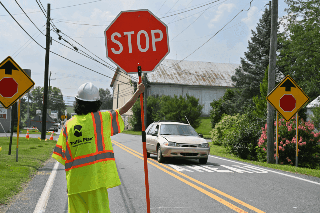 traffic control flagger holding a stop sign with a small car approaching