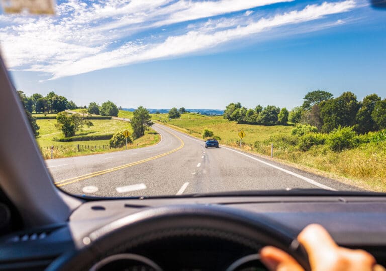 first person image of person driving a car with a blue sky background with green grass and trees