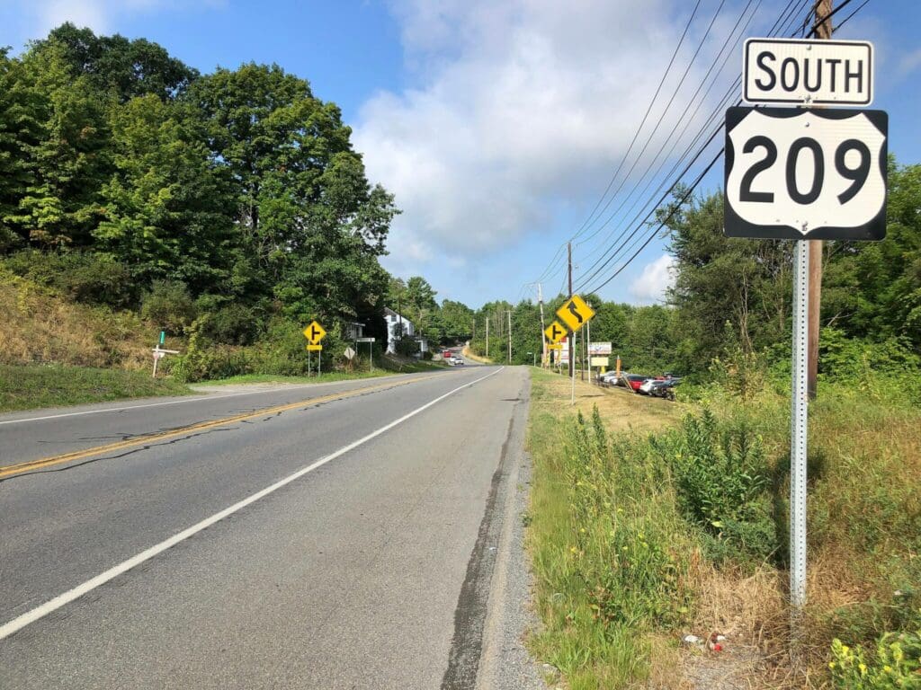 highway with south 209 sign posted on the right sitting beneath a blue sky with white clouds