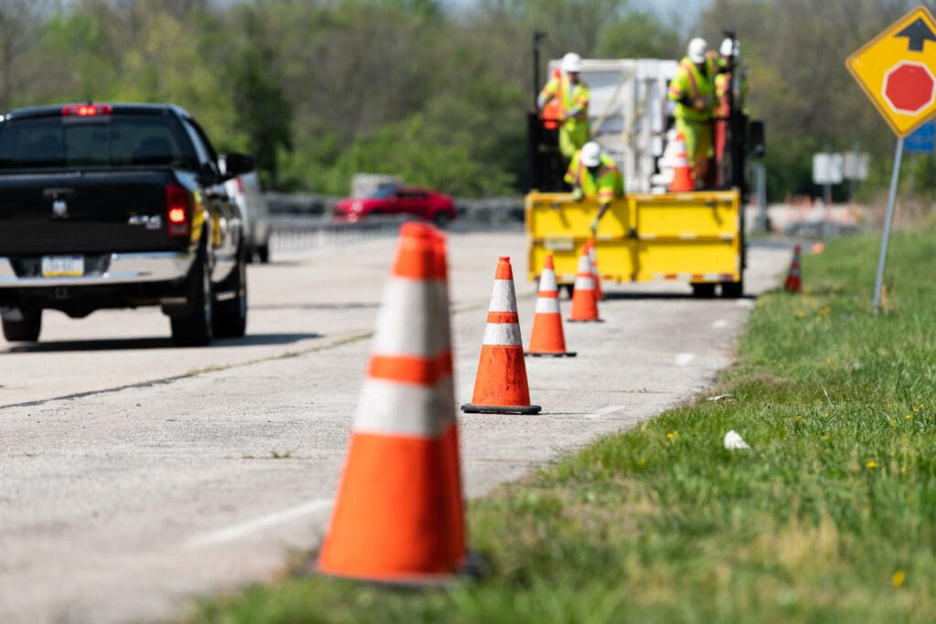 orange traffic cones lined up beside a highway with a black dodge ram driving by them