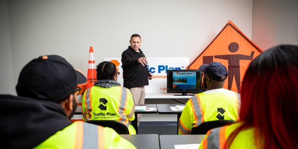 instructor teaching traffic plan crew member in classroom with company logo and flagger sign behind him